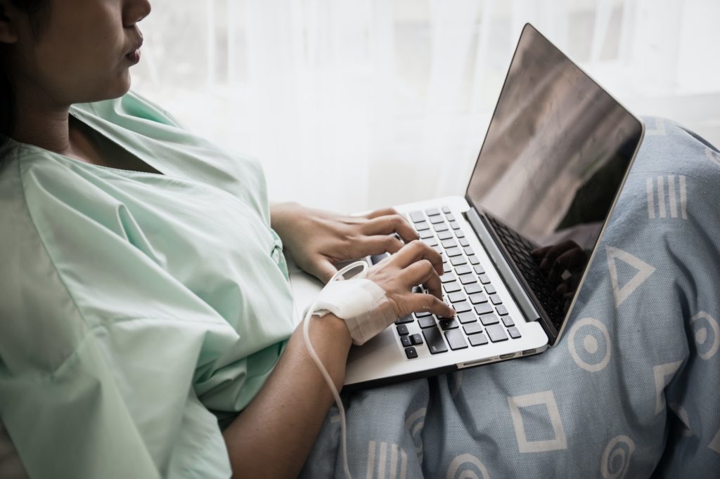 Sick woman works with laptop in hospital.